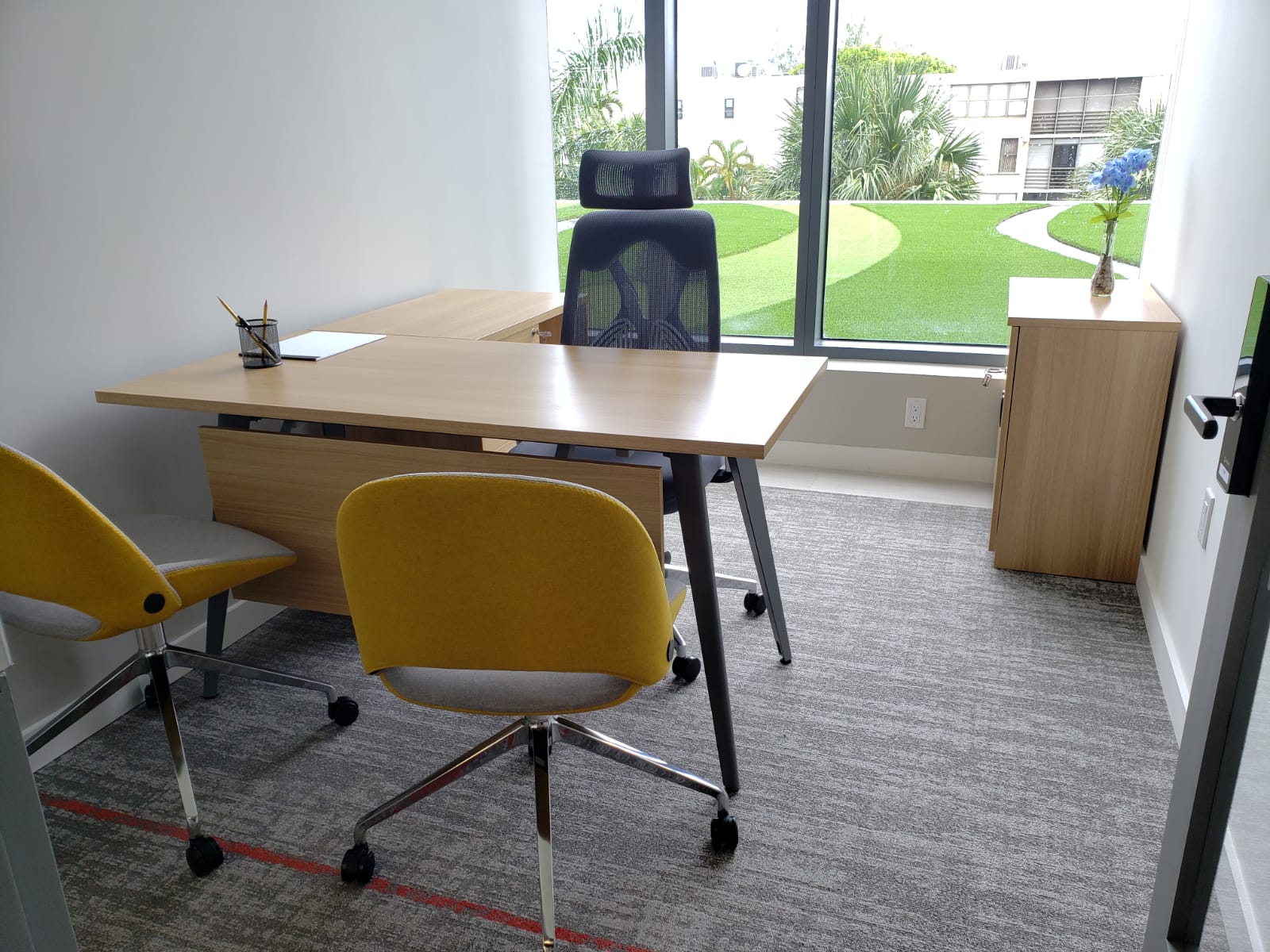 Individual exterior private office with wooden desk and yellow chairs overlooking a garden