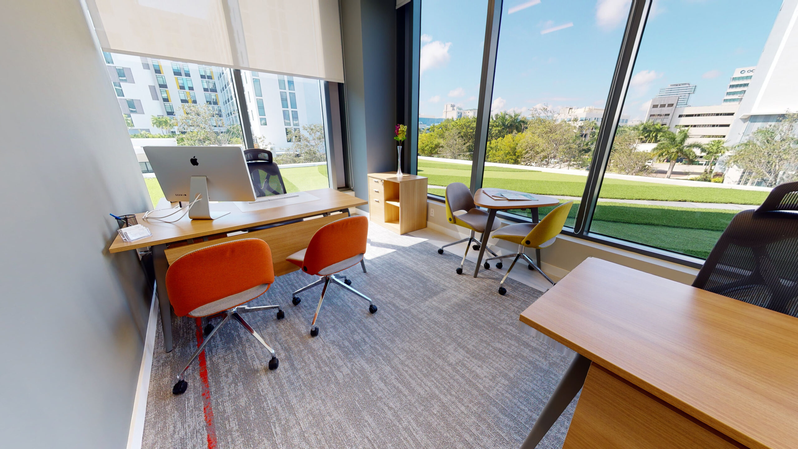 Private office with wooden desk, orange chairs and bright window view
